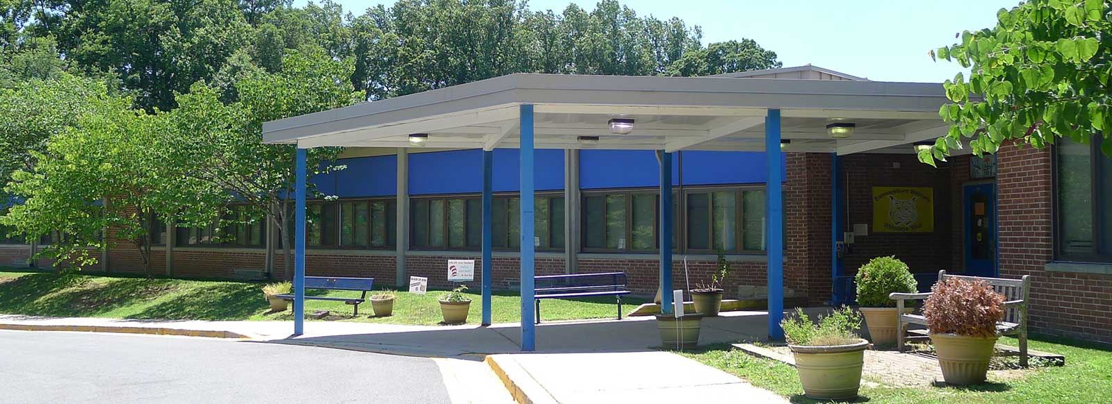 The covered front entrance of Bannockburn Elementary School, with blue columns, benches and planters